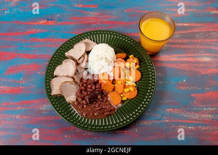 Piatto tipico brasiliano con riso, fagioli rossi, insalata di maiale e carote e mais brasato in un piatto verde Foto Stock