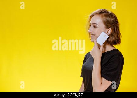 Giovane donna sorridente che tiene la carta di credito su sfondo giallo Foto Stock