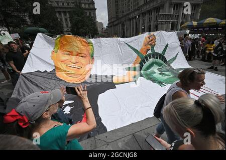 Le folle si riuniscono intorno a un grande banner raffigurante il sindaco di New York Bill de Blasio che tiene la testa tagliata della Statua della libertà mentre l'agrode dei manifestanti tiene un rally fuori dal municipio contro le vaccinazioni COVID-19 e i mandati per le persone di essere vaccinate, New York, NY, 9 agosto 2021. New York sarà la prima città a vietare le persone non vaccinate da ristoranti, palestre e locali di intrattenimento al coperto a partire dal 16 agosto, con attuazione a partire dal 13 settembre; la variante Delta del Coronavirus ha causato un aumento delle infezioni COVID-19 in tutti gli Stati Uniti, soprattutto tra i non vaccinati Foto Stock