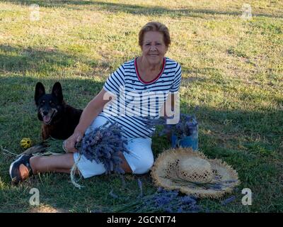 ritratto signora oltre 65 con un bouquet di lavanda e un cane al suo fianco Foto Stock