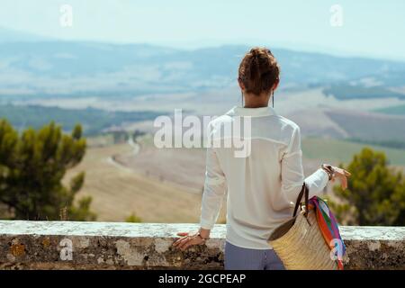 Viaggi in Italia. Vista da dietro elegante donna turistica solitaria con sacco di paglia che ha fatto un tour a piedi a Pienza in Toscana, Italia. Foto Stock