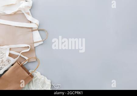 Posa piatta con sacchetti di carta da artigianato eco bianco e sacchetti a rete su sfondo grigio con spazio di copia vuoto area pubblicitaria. Modello di imballaggio. Consegna Foto Stock