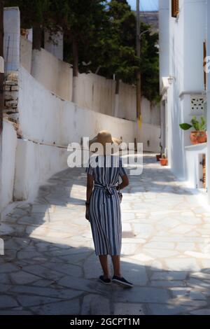 Una ragazza cammina nella città vecchia di Athen, Grecia. La giovane donna cammina con un cappello di paglia e un abito a righe in estate attraverso Atene. Una calda giornata estiva in t Foto Stock