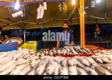 Mercato notturno Street food a Putrajaya, vicino a Kuala Lumpur. Venditore con maschera facciale in un negozio di pesce di strada. I pesci sono sdraiati sul bancone in avanti Foto Stock