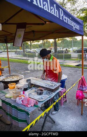 Giovani uomini frittura Youtiao o Cakoi, una lunga striscia di pasta fritta in oro-marrone. Su un mercato fresco in Malesia cucina all'aperto Foto Stock