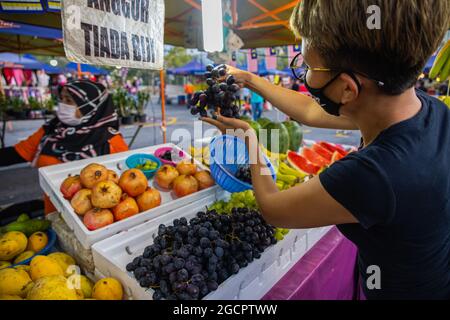 La giovane malasica controlla la qualità delle uve prima dell'acquisto. La ragazza indossa la maschera facciale a causa della crisi del virus. Mercato fresco o umido in Foto Stock