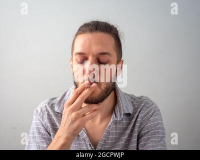 L'uomo caucasico in camicia grigia fuma una sigaretta in stanza bianca a Medellin, Colombia Foto Stock