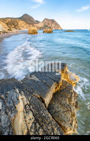 Onde che si infrangono contro rocce, spiaggia sabbiosa con scogliere rocciose, Paralia Paradisos, Kos, Dodecanese, Grecia Foto Stock