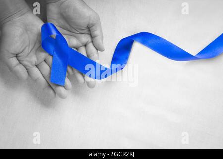 Mani che tengono il nastro blu profondo su tessuto bianco con spazio per la copia. Consapevolezza del cancro colorettale, cancro del colon della persona anziana e giornata mondiale del diabete, Chil Foto Stock