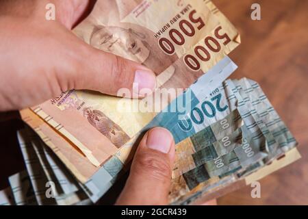 Mano maschile tenere un ventilatore Indonesia rupiah banconota, la valuta dell'Indonesia. Primo piano sul denaro sporco di carta dell'Indonesia. L'uomo mostra un fan dell'Indonesia Foto Stock