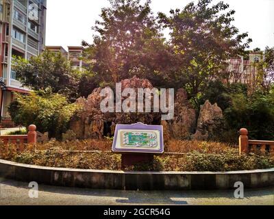 Una piccola area giardino con un masso scosceso, alberi verdi, fiori e un cartello con la mappa nel quartiere di Nanxi Foto Stock