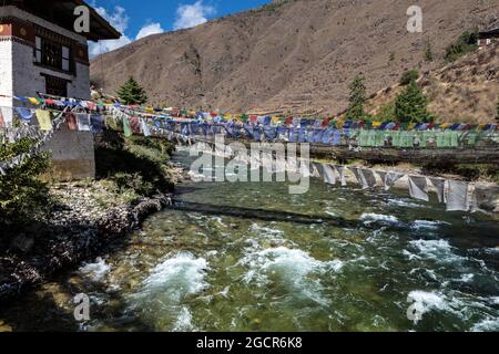 Il paesaggio montano del Bhutan, il fiume Paro Chu accanto all'autostrada Paro - Thimphu. Un ponte sospeso a piedi su un fiume di montagna con colorfu Foto Stock