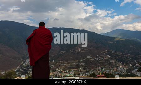 Un monaco in una tana rossa si affaccia sul paesaggio montano del regno del Bhutan vicino alla città di Paro. Foto Stock