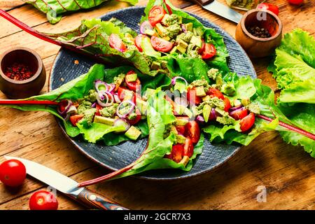 Insalata di avocado, pomodoro con salsa all'aglio in foglie di bietole. Insalata di vitamina estiva in piatto Foto Stock