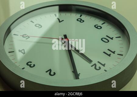 Orologio da parete bianco moderno mostra il tempo 5 dopo il 12. Avvicinati a un orologio da parete alla luce del sole con ombre sul quadrante dell'orologio. Il tempo è scaduto. Sono cinque Foto Stock