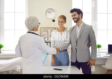Felice giovane coppia scuotendo le mani con il loro medico di famiglia o specialista di gravidanza Foto Stock