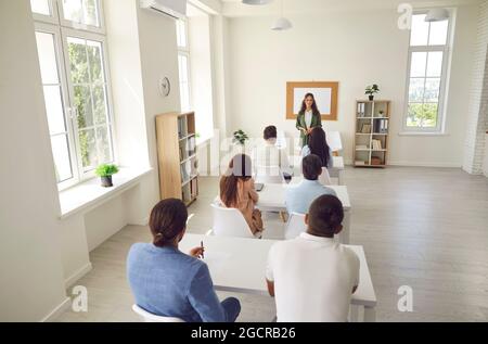 Gruppo di studenti adulti che hanno una lezione seduto alle scrivanie in un moderno interno dell'aula Foto Stock