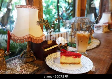Cheesecake alla fragola servita con un bicchiere di caffè latte ghiacciato in una caffetteria d'epoca decorata con mobili antichi in legno Foto Stock
