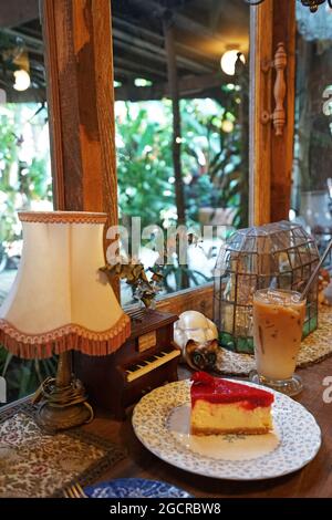 Cheesecake alla fragola servita con un bicchiere di caffè latte ghiacciato in una caffetteria d'epoca decorata con mobili antichi in legno Foto Stock