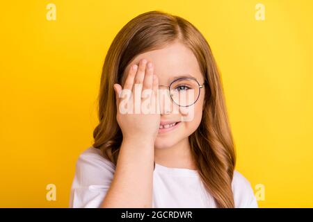 Foto di giovane bambina felice positivo sorriso copertura occhio mano check-in visione oculista isolato su sfondo giallo Foto Stock