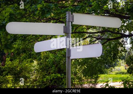 Cartello di direzione vuoto in un parco pubblico. Palo freccia vuota che punta la strada all'esterno in una giornata di sole. Foto Stock