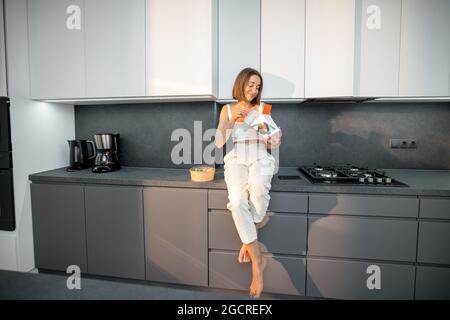 Donna mangia cibo da asporto in cucina moderna Foto Stock