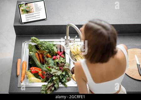 Donna che cucina con verdure fresche e verdure nel lavello Foto Stock