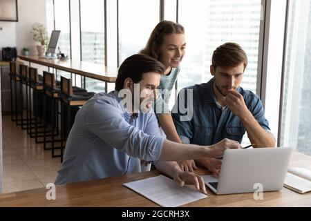 Gruppo creativo che lavora in ufficio insieme, condividendo il laptop Foto Stock