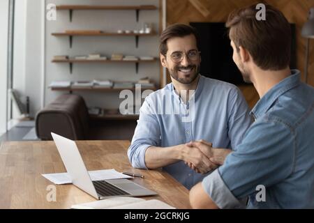 Due uomini d'affari felici e sicuri che scuotono le mani sul posto di lavoro Foto Stock