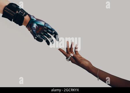 Protesi di mano maschile cyborg che raggiunge la mano nera africana umana femminile. Concetto di avanzamento del contatto con le mani Foto Stock