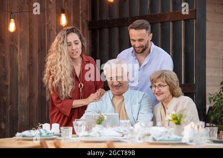 Due coppie che comunicano tramite chat video con i loro amici dopo la cena in famiglia Foto Stock