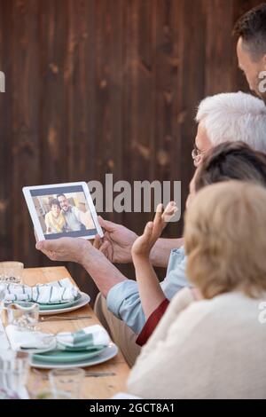 Una delle donne che agita la mano a una giovane coppia sul display del tablet durante la comunicazione online Foto Stock