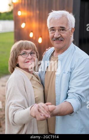 Felice uomo anziano e donna che tiene per mano davanti alla macchina fotografica all'aperto Foto Stock