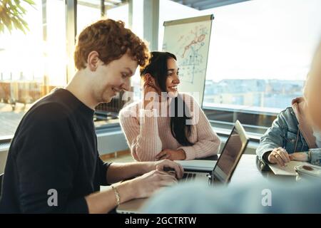 Giovane sorridente che lavora su un computer portatile all'università con amici seduti accanto. Studenti che hanno uno studio di gruppo nella scuola superiore. Foto Stock