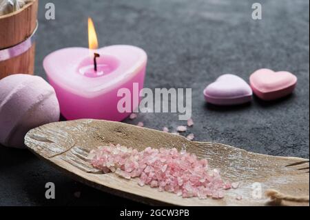 SPA Still Life, bombe da bagno a forma di cuore rosa, sale con candela illuminata su fondo di cemento. Disposizione piatta, vista dall'alto Foto Stock