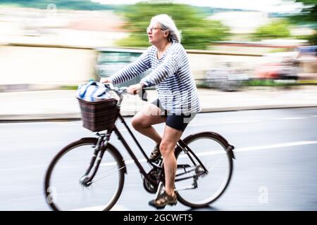 Donna di mezza età o anziana in bicicletta con sfocatura della velocità. Bath Spa, Somerset, Regno Unito Foto Stock