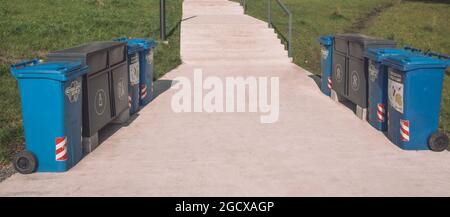 Marciapiede in parco con bidoni di riciclaggio rifiuti per rifiuti ordinati da lati sul prato. Stile di vita sostenibile in ambiente urbano. Conservazione ambientale Foto Stock