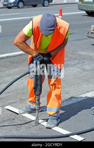 Lavoratore che si prepara a stendere per asfaltare la strada sulla strada utilizzando un demolitore pneumatico. Foto Stock