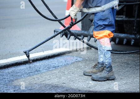 Il lavoratore posare il bitume usando l'irroratrice di catrame, in piedi davanti ad una macchina spruzzatrice di bitume. Foto Stock