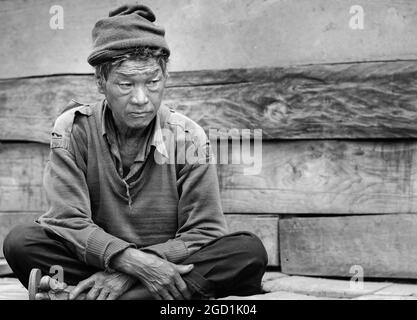 Ritratto dell'uomo anziano della tribù etnica Sherdukpen seduto fuori casa con triste espressione vicino Tawang, India. Foto Stock