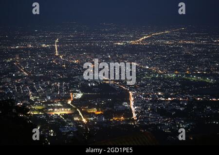 Vista mozzafiato delle luci notturne di una grande città (Chiang mai) da una collina vicina Foto Stock