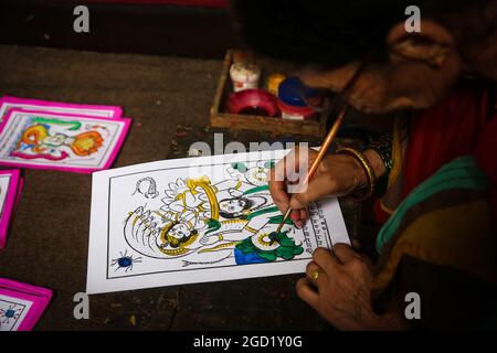 Bhaktapur, Bagmati, Nepal. 10 agosto 2021. Chet Kumari Chitrakar, 68, popolarissimo conosciuto come ''creatore degli dei'', dà il tocco finale all'immagine tradizionale per il festival di Nag Panchami, un festival indù per adorare la divinità serpente a Bhaktapur, una città conosciuta anche come ''˜la città dei devoti' in Nepal il 10 agosto 2021. Chet Kumari Chitrakar e la famiglia continuano a fare tali immagini di stampa a mano per molti festival, nonostante la minore domanda a causa dell'interesse della gente nelle moderne immagini di stampa a macchina. Le famiglie di Chitrakar sono conosciute basicamente come pittori e scultori in Nepal che hanno rappresentato gli dei e g Foto Stock