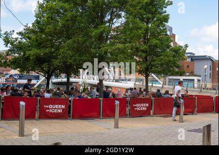 Regina di Iceni fuori tavoli e sedie con persone sedute a mangiare e bere con il ponte di amicizia Novi Sad sullo sfondo Foto Stock