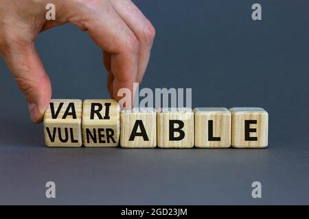 Simbolo vulnerabile o variabile. L'uomo d'affari gira i cubi di legno e cambia la parola vulnerabile a variabile. Splendido sfondo grigio, spazio per la copia. Busi Foto Stock