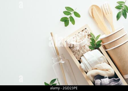 Buste ecofiendly a posa piatta, tazze di carta, posate di bambù, bottiglia d'acqua di galss con foglie verdi su sfondo bianco. Foto Stock