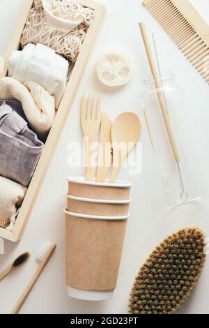 Accessori ecologici su sfondo bianco. Set di sacchetti eco, tazze di carta, posate di bambù, pettine per capelli, spazzola per il corpo, bottiglia d'acqua. Disposizione piatta, vista dall'alto. Foto Stock