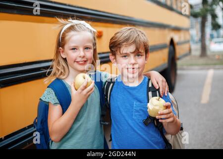 Bambini ragazzi e ragazze studenti amici mangiare mele snack sano da scuola bus giallo all'aperto. Istruzione e ritorno a scuola nel mese di settembre. Compagno di classe Foto Stock