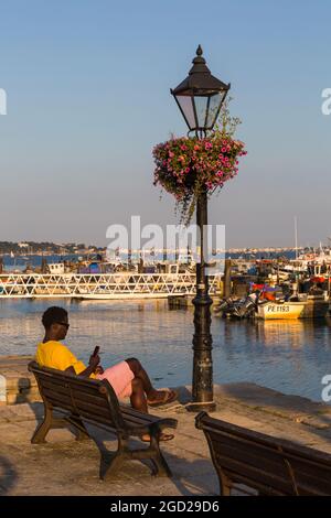 Uomo seduto in panchina rilassante in serata con le barche ormeggiate a Poole Quay a Poole Harbour, Poole, Dorset UK nel mese di luglio Foto Stock