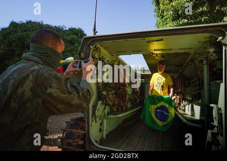 Brasilia, Brasile. 10 agosto 2021. Un soldato usa un telefono cellulare per fotografare un sostenitore di Bolsonaro che tiene una bandiera del Brasile in un veicolo militare ai margini di una parata militare. Credit: Myke Sena/dpa/Alamy Live News Foto Stock