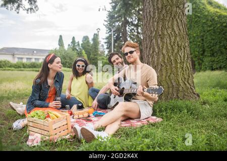 Quattro amici con la chitarra al picnic nel parco Foto Stock